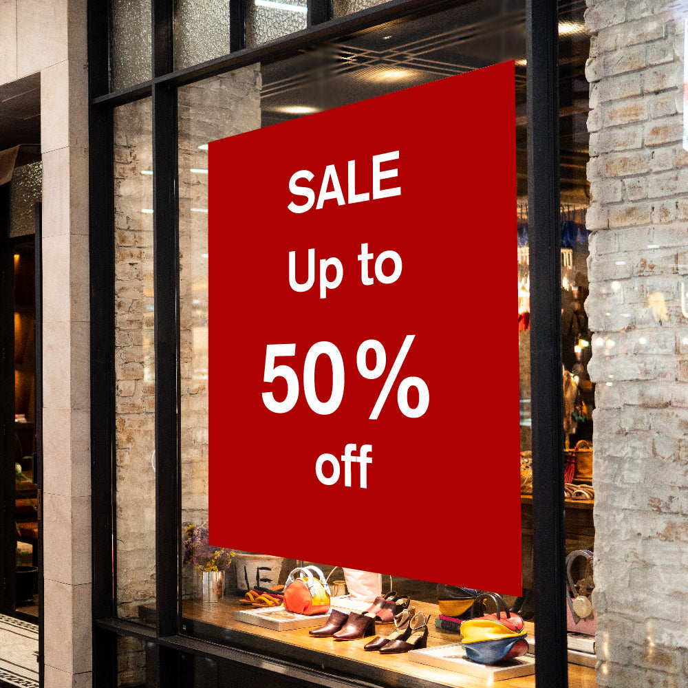 Red sale sign in a store window advertising up to 50% off.