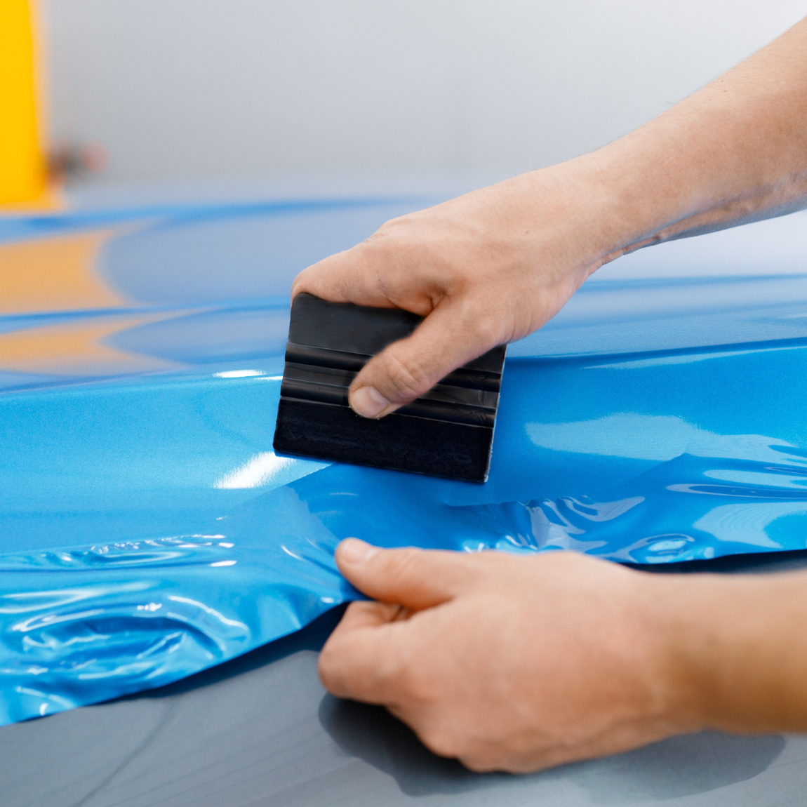 Person applying a blue car wrap to a vehicle with a squeegee
