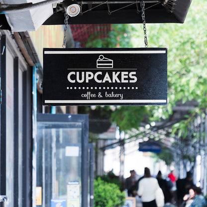Sign for Cupcakes coffee & bakery hanging above a street with people walking by.
