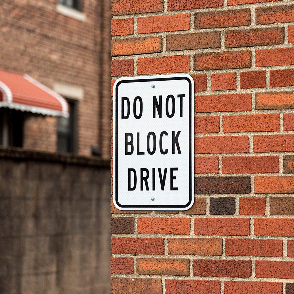 Street sign on a brick wall warning 'Do Not Block Drive'.